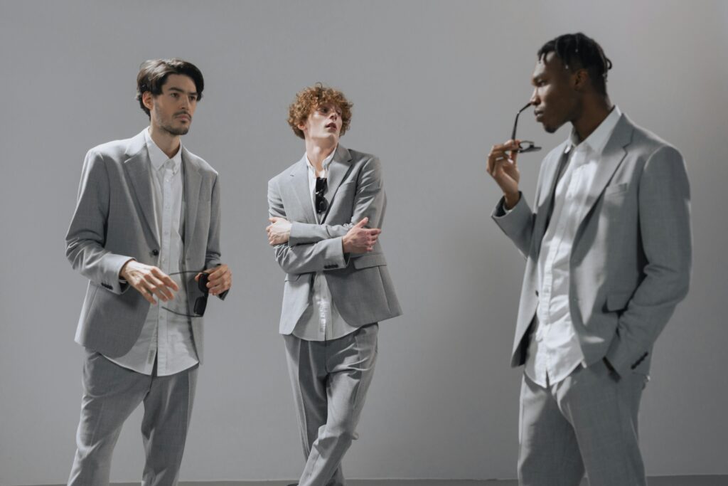 Three diverse young professionals in gray suits posed casually indoors.